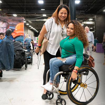 Smiling woman standing beside a smiling woman in a wheelchair